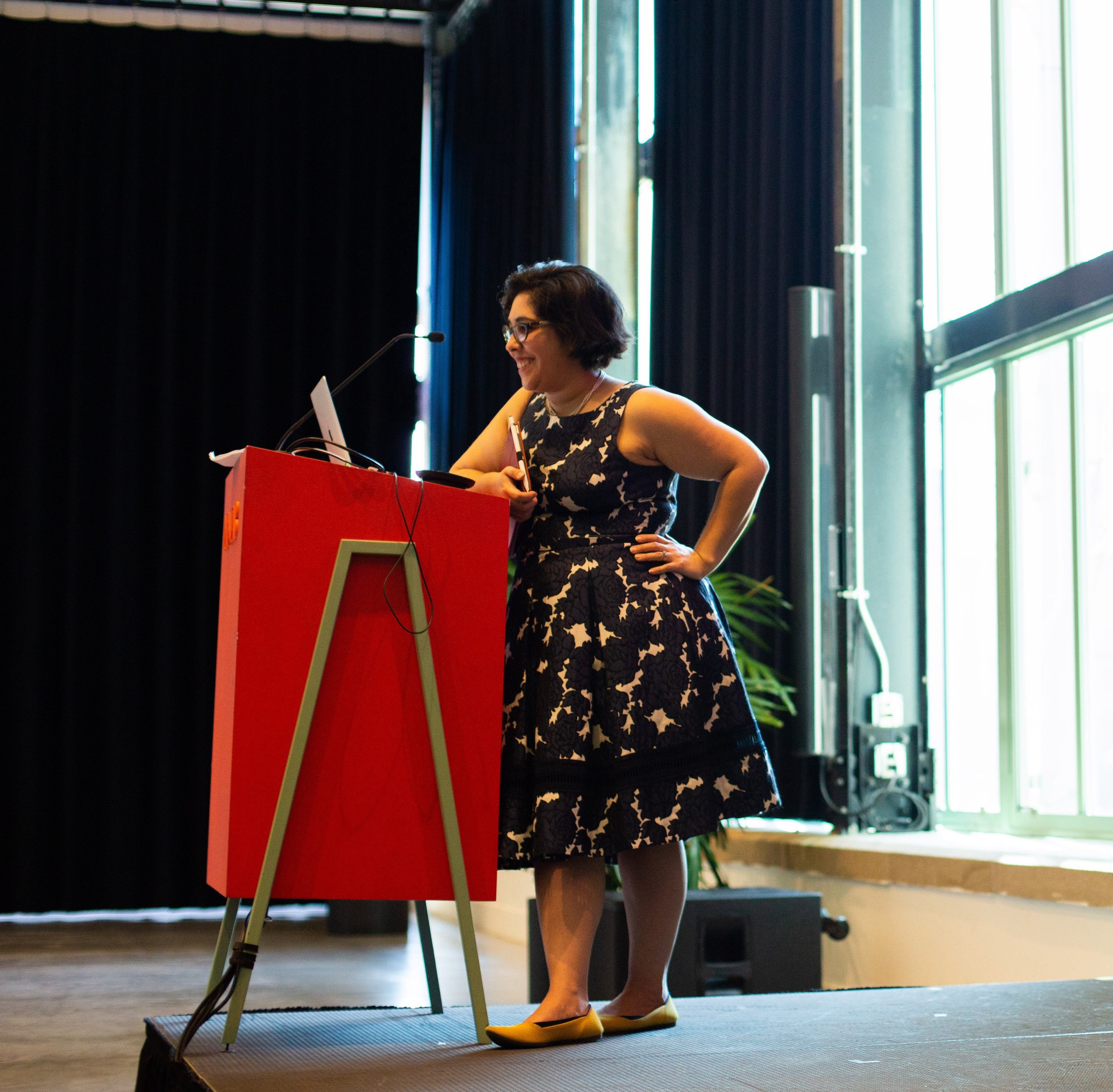 Woman standing at red podium, hand on hip, smiling