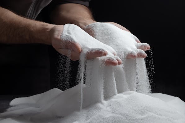 Close-up of a person’s hands with fingers spread apart, letting fine white sand cascade down smoothly between them, against a dark background, creating a striking visual contrast and a sense of time slipping away.