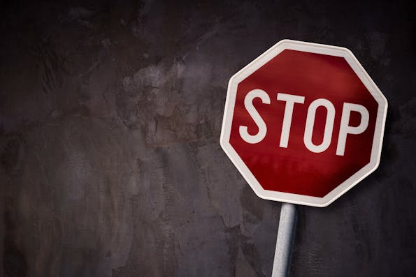 A red stop sign stands out against a textured, dark grey background, with bold white letters commanding attention and signaling the universal message to halt.