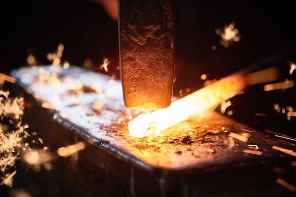 Close-up of a glowing piece of metal being worked upon with a hammer on an anvil, sparks flying in all directions, capturing the heat and intensity of metal forging.