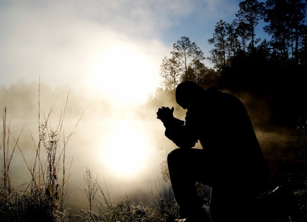 A silhouette of a person in prayer, kneeling with hands clasped against a backdrop of a misty, sunlit morning. The rising sun filters through the haze, enveloping the figure in a soft glow, creating an atmosphere of tranquility and devotion.