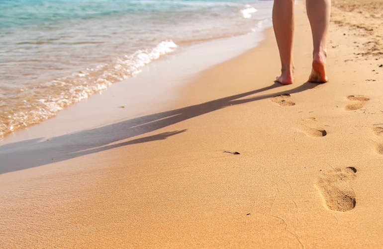 Legs walking along a beautiful seashore and leaving footprints in the sand